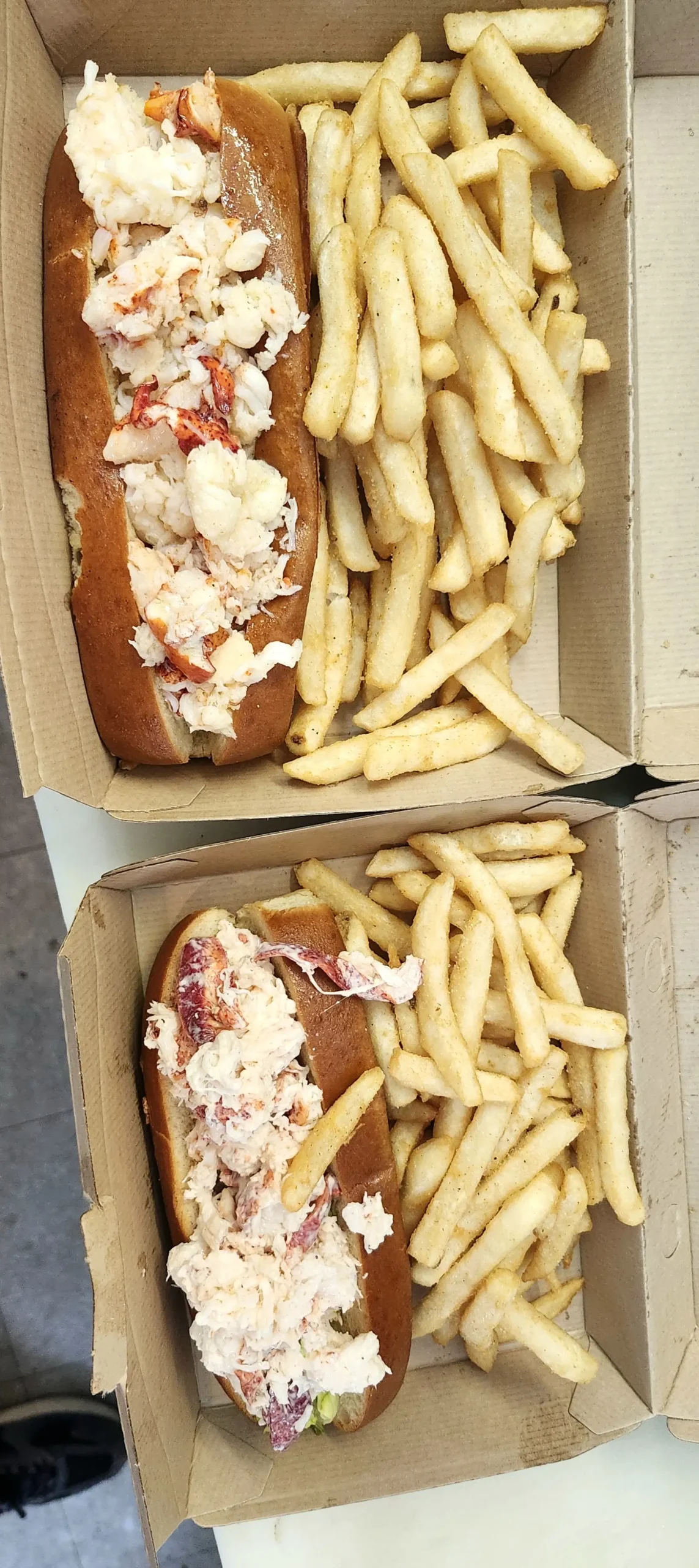 Two lobster rolls with fries in takeout boxes